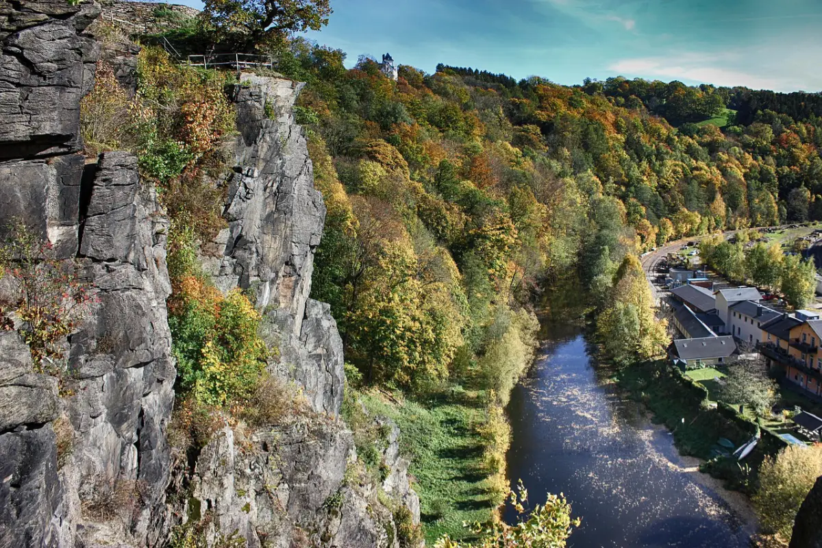 Bei herbstlicher Blätterfärbung thront eine Aussichtsplattform an einer Felswand über einem Fluss.